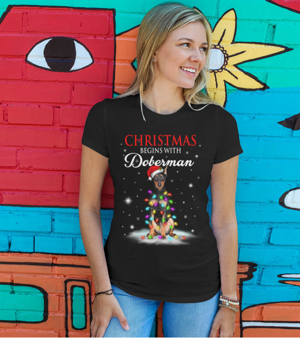 Christmas Begins With Doberman Wrapped In Holiday Lights And Santa Hat Snowflakes T-Shirt